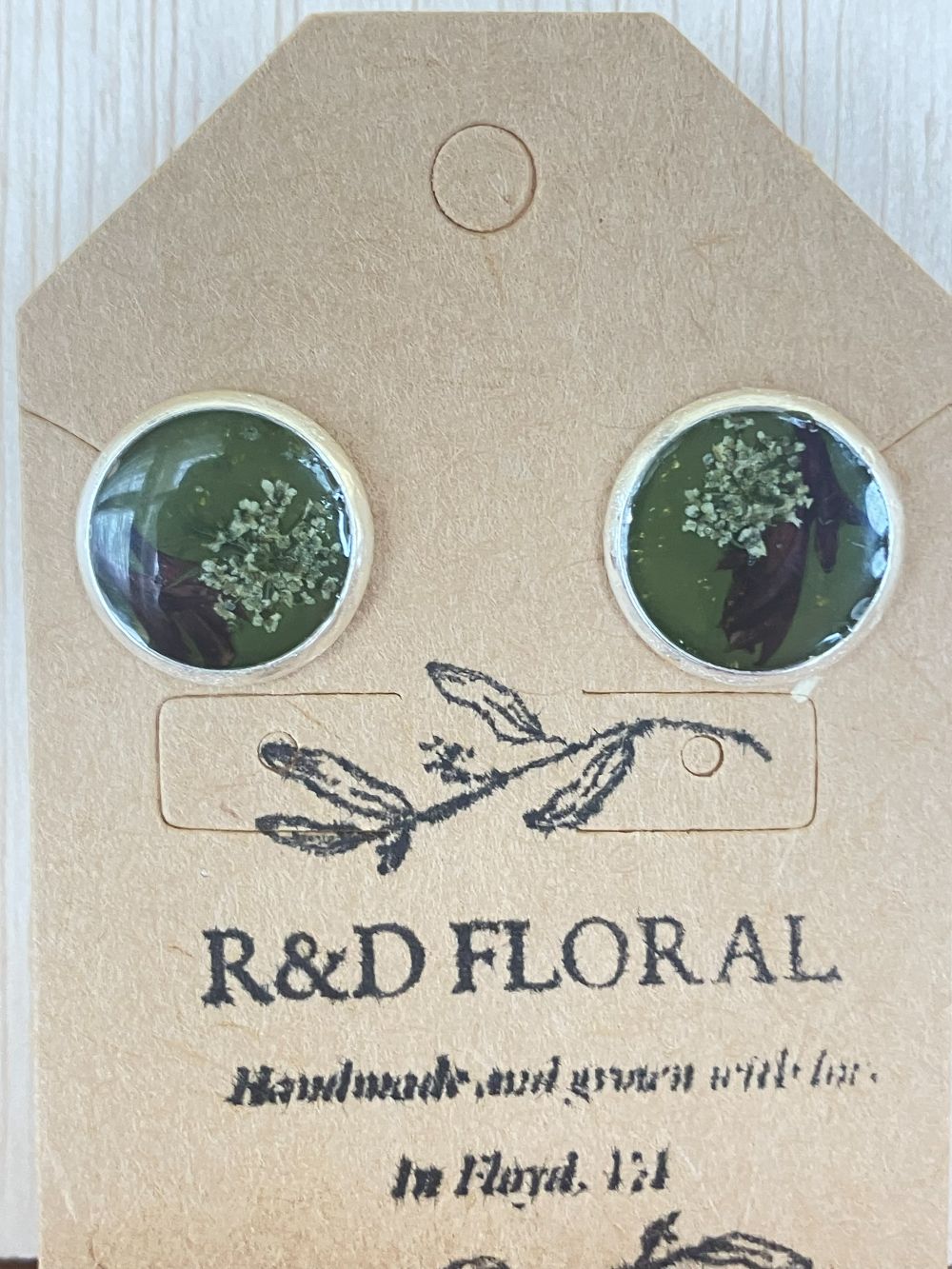 Silver metal stud earrings with olive green resin encasing Queen Anne’s Lace and Bachelor button petals handmade by R & D Floral.